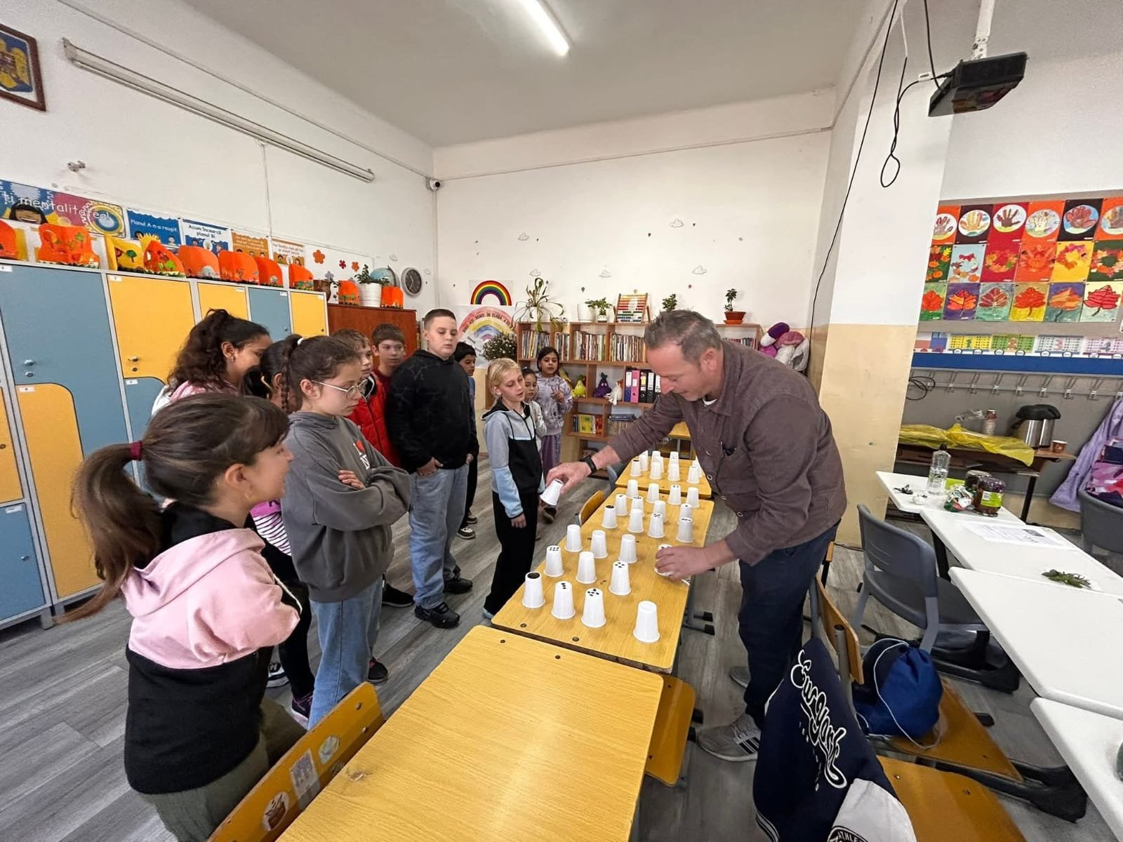 Grup de elevi participanți la un joc educativ cu pahare, coordonați de un profesor în cadrul proiectului „Culorile toamnei – Atelier de creație și tradiție"