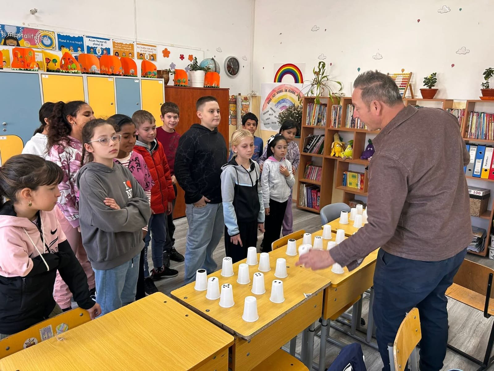 Elevi adunați în jurul profesorului, urmărind demonstrarea unui joc interactiv cu pahare, parte din atelierul educativ de toamnă.