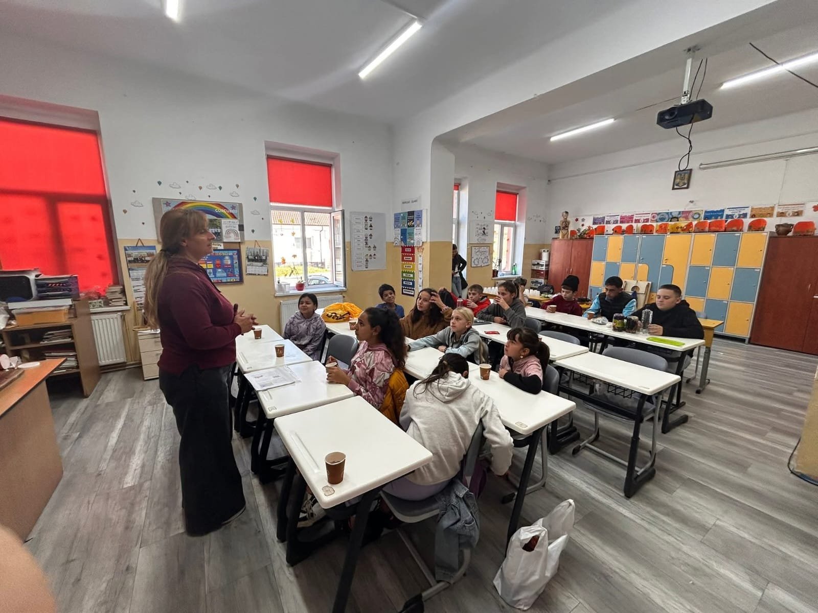 Cadru didactic explicând elevilor activitățile atelierului „Culorile toamnei”, într-o sală decorată cu lucrări tematice.