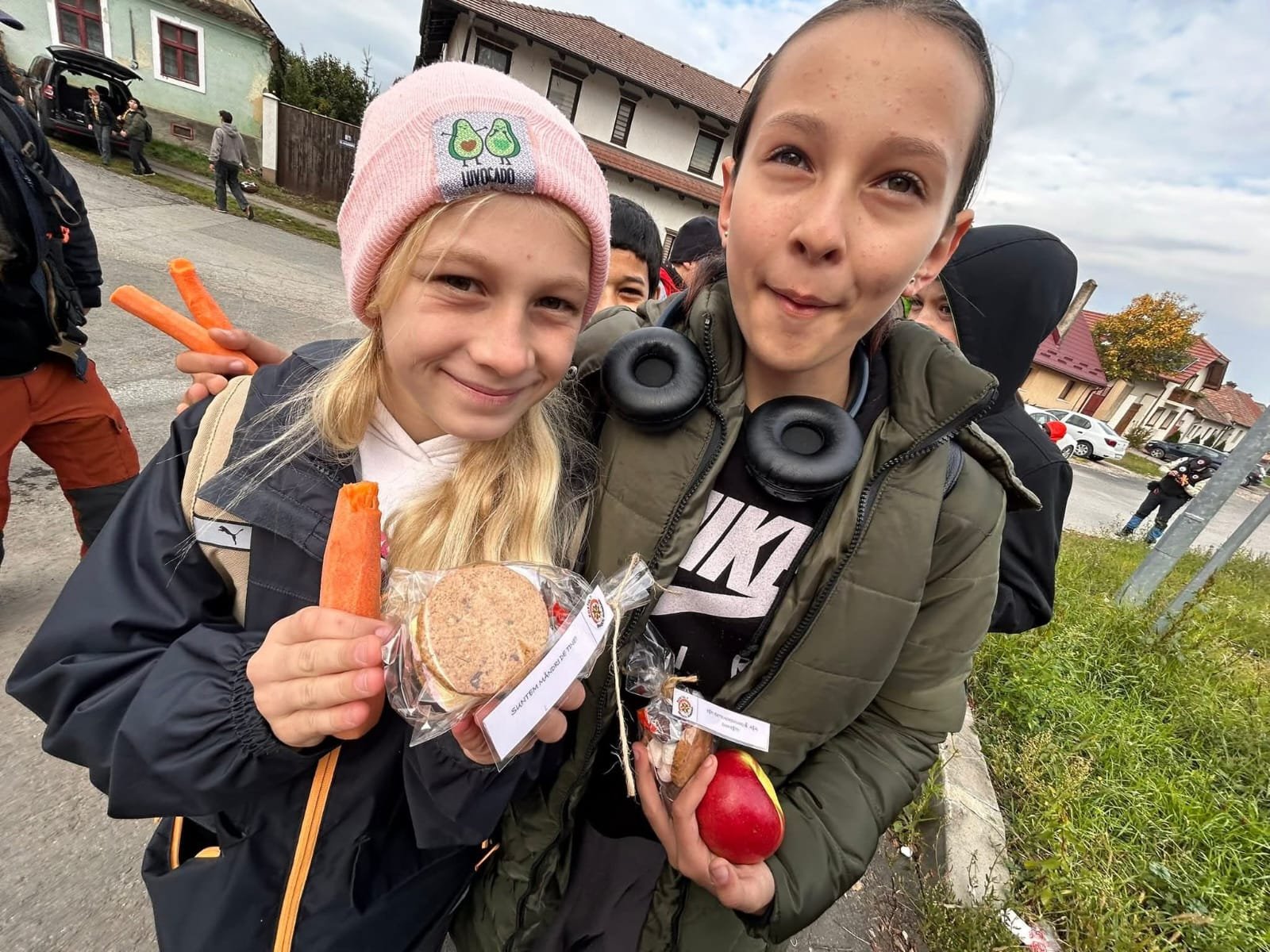 Două eleve ținând morcovi, fructe și pachete educative în timpul excursiei Recunoștință în Natură.