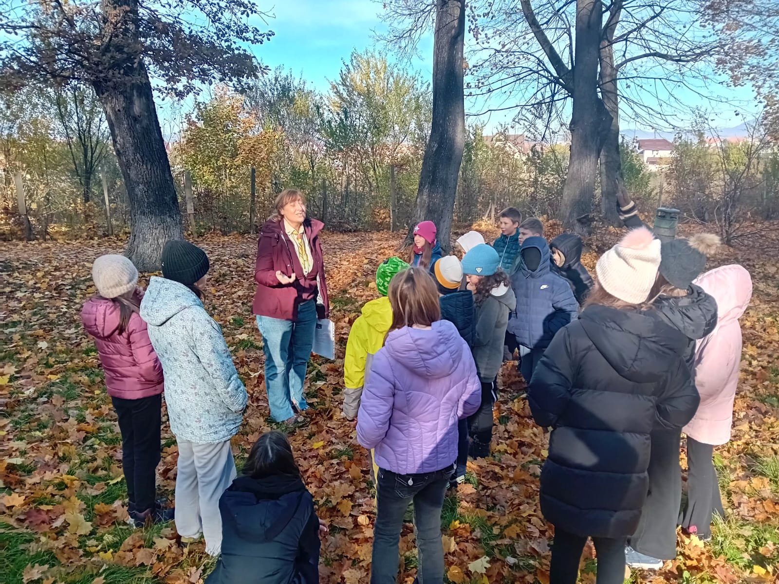 Formator ACPEIO explicând tema recunoștinței unui grup de elevi, într-o poiană acoperită de frunze de toamnă, la Râșnov.