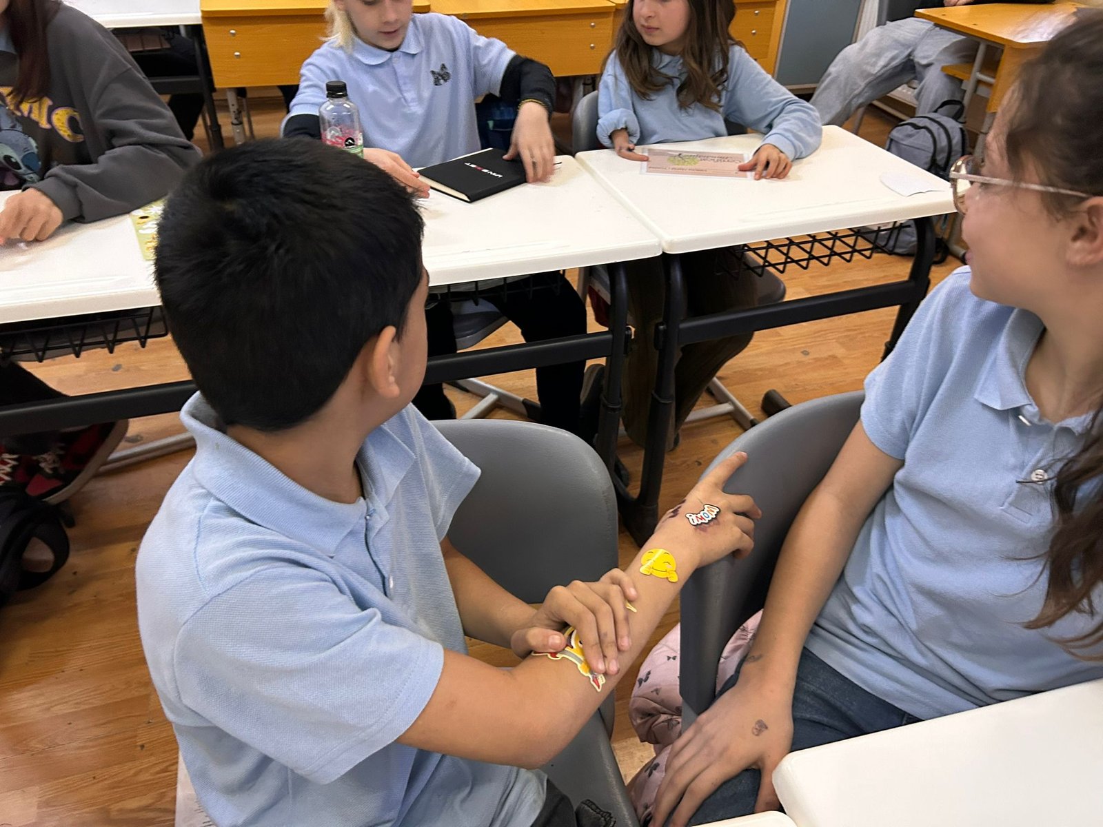Doi elevi își lipesc stickere cu emoticoane pe brațe și discută, în cadrul unui exercițiu de exprimare non-verbală a emoțiilor.