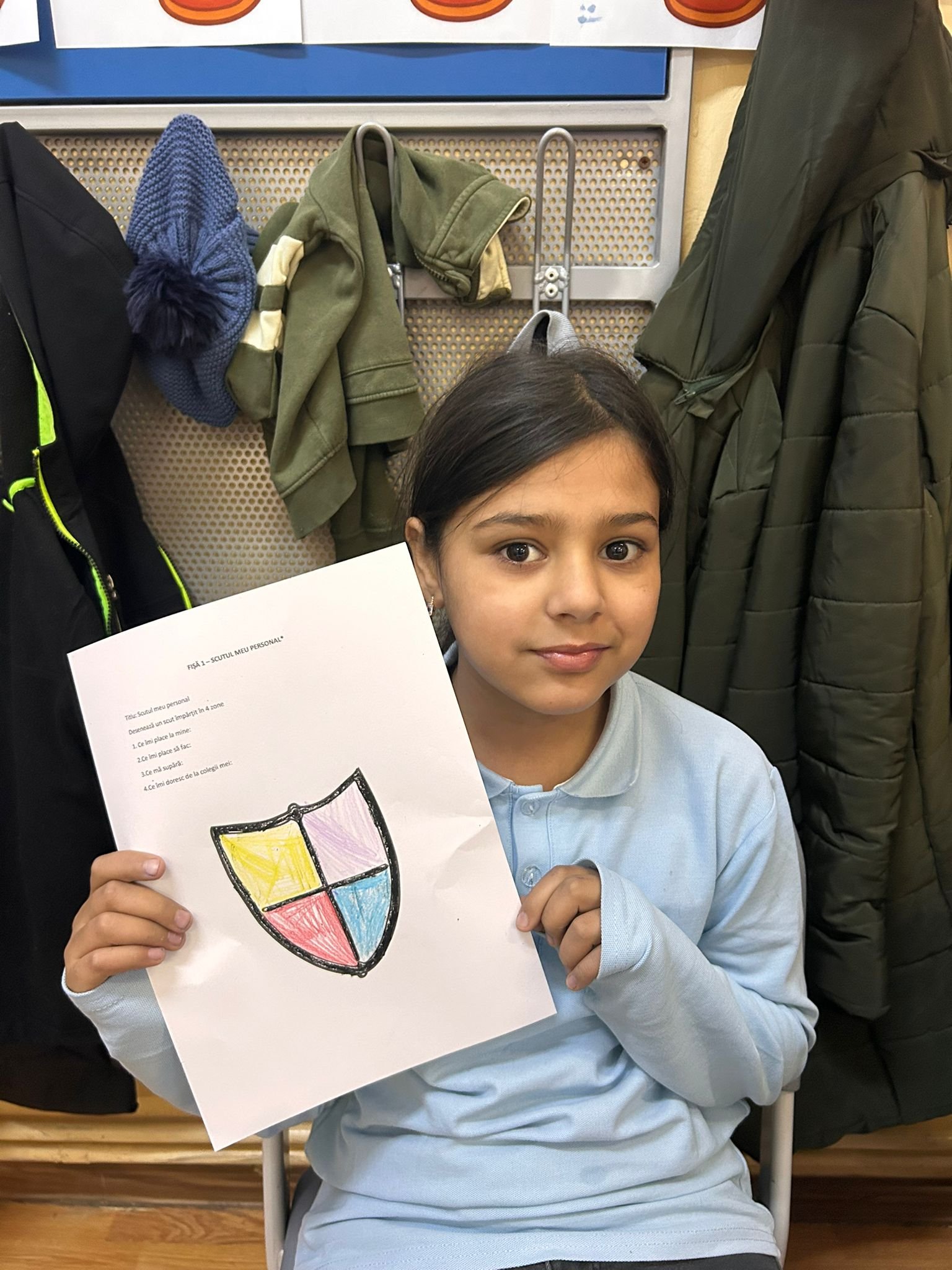 Fetiță în uniformă albastră își prezintă foaia cu „Scutul meu personal”, colorat în patru zone, parte din exercițiile de autocunoaștere din programul „Scânteia schimbării”.
