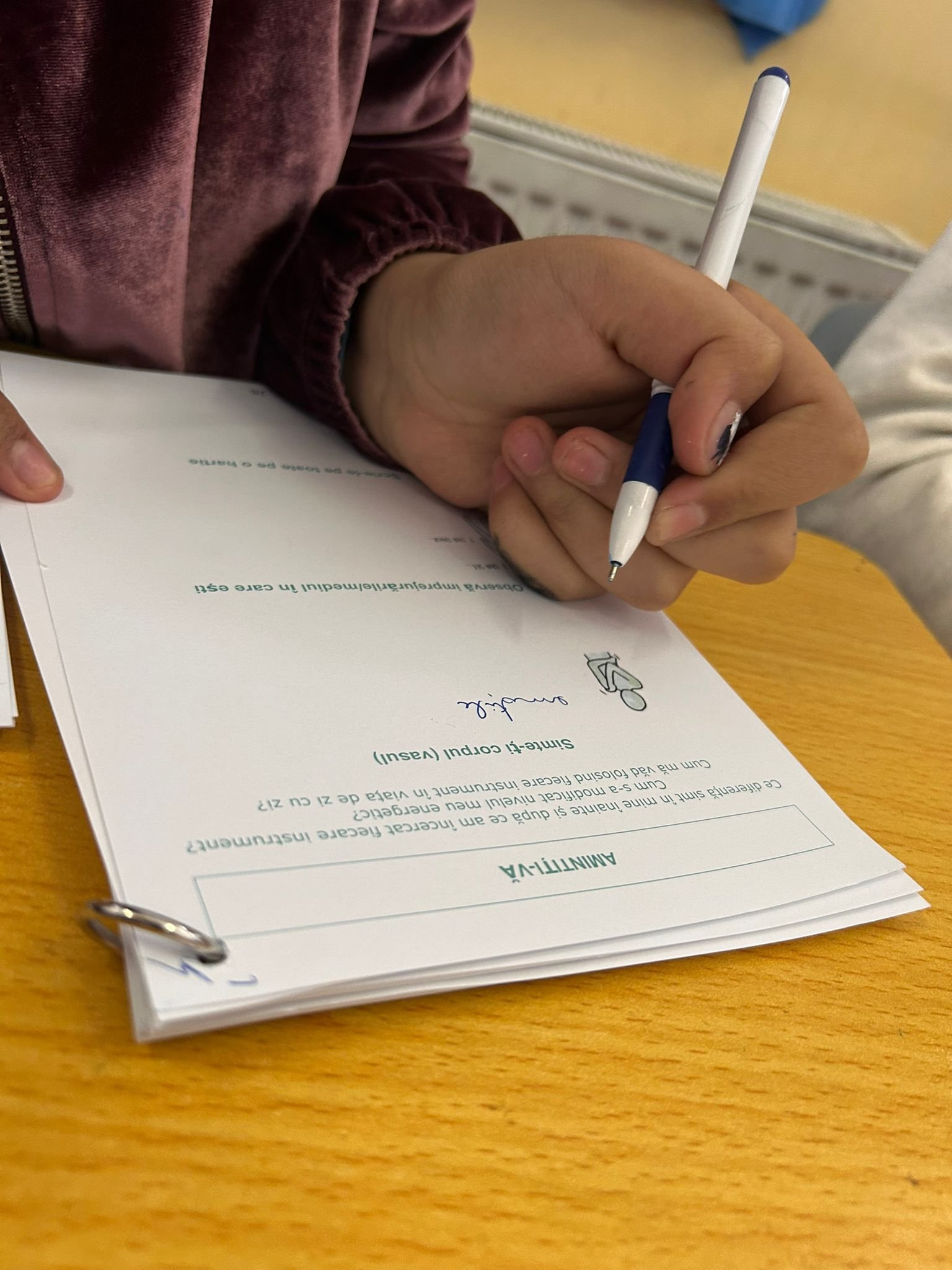 Mână de elev scriind într-un caiet de lucru First Aid Arts, în cadrul lecției despre reziliență la Școala Gimnazială Bod.