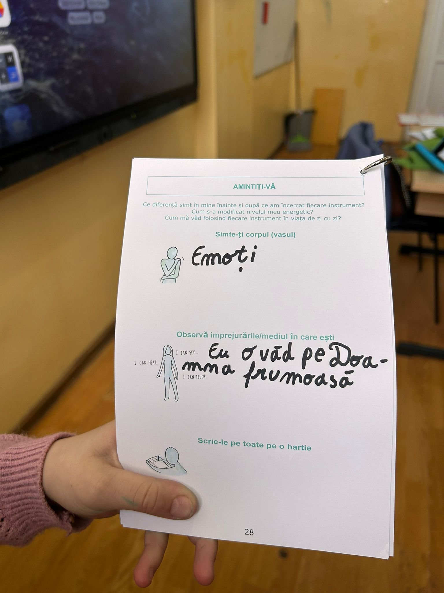 Pagina completată de un elev, cu exercițiul despre emoții și observarea mediului, ținută în mână în sala de clasă.