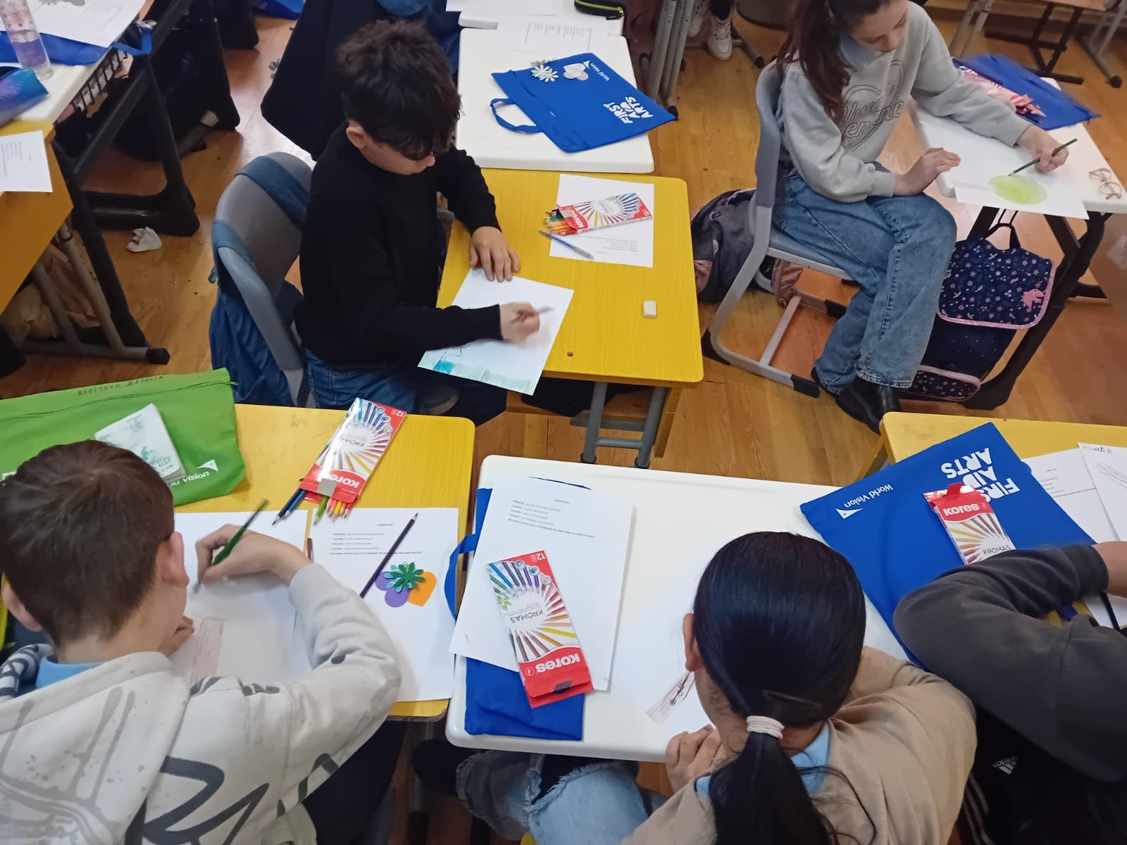 Copil care desenează un copac la activitatea Arta ca medicament pentru suflet, cu creioane colorate și materiale First Aid Arts pe bancă